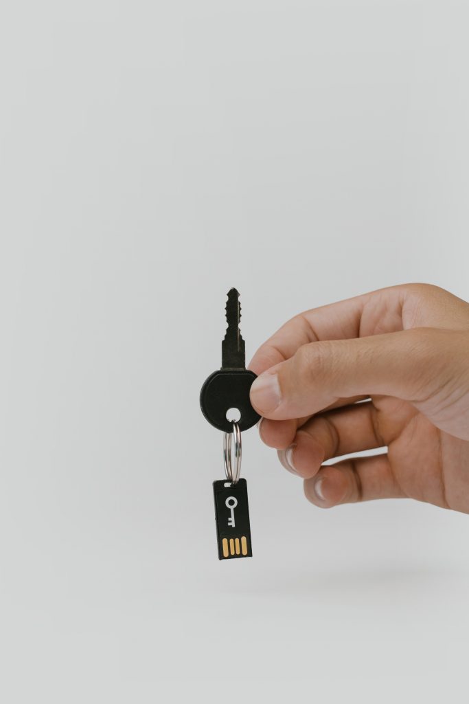 Male right hand holding a key with a chip key chain in front of a light grey background.